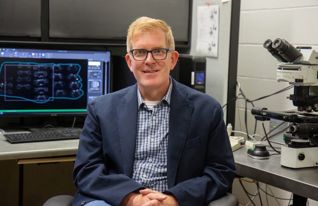 David Kline poses for portrait by microscope. 