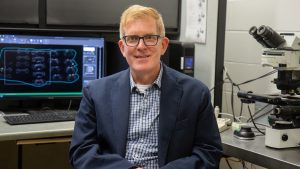 David Kline poses for portrait by microscope.